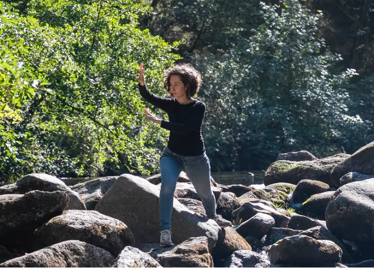 Giorgia Ciampi Tsolaki in a Taiji stance on river rocks with woodland behind