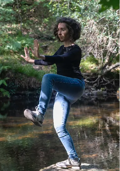 Giorgia Ciampi Tsolaki balancing on one leg in a Taiji posture beside a woodland river