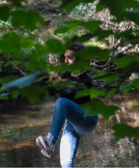 Giorgia Ciampi Tsolaki in a one-legged Taiji stance, seen through leaves by a river