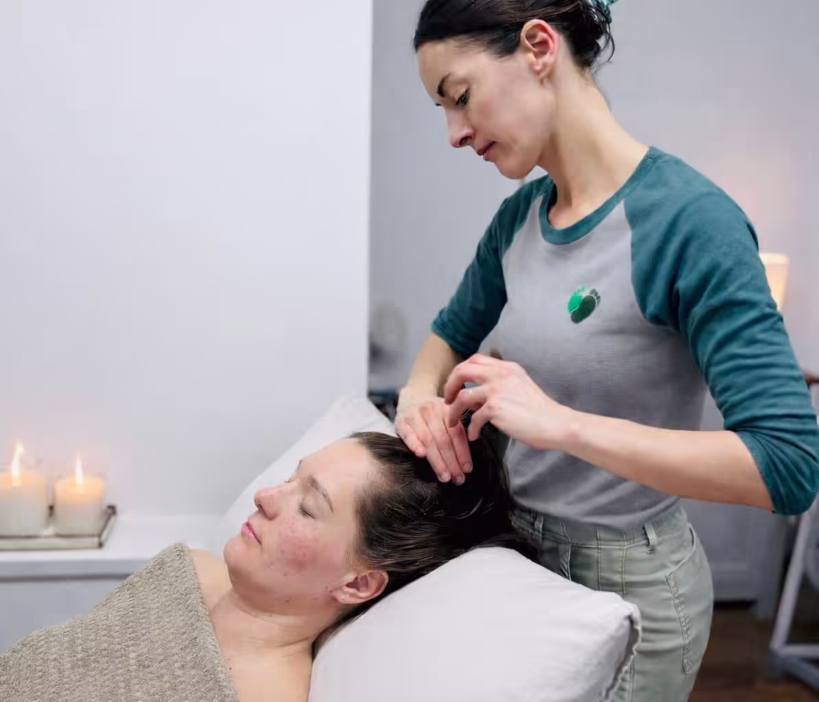 Massage therapist gently massaging a client’s scalp by candlelight in a calm treatment room