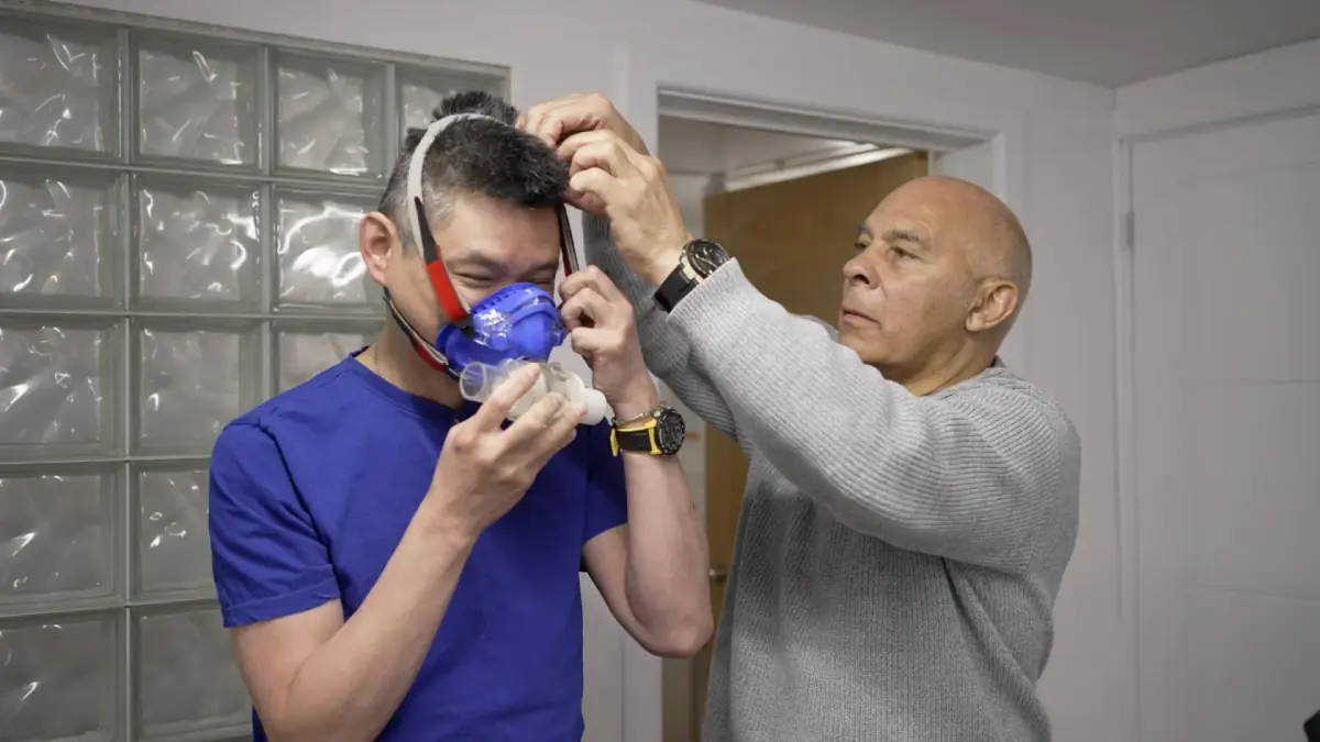 Tester adjusting the head straps of a breath-analysis mask on a client before a metabolic assessment
