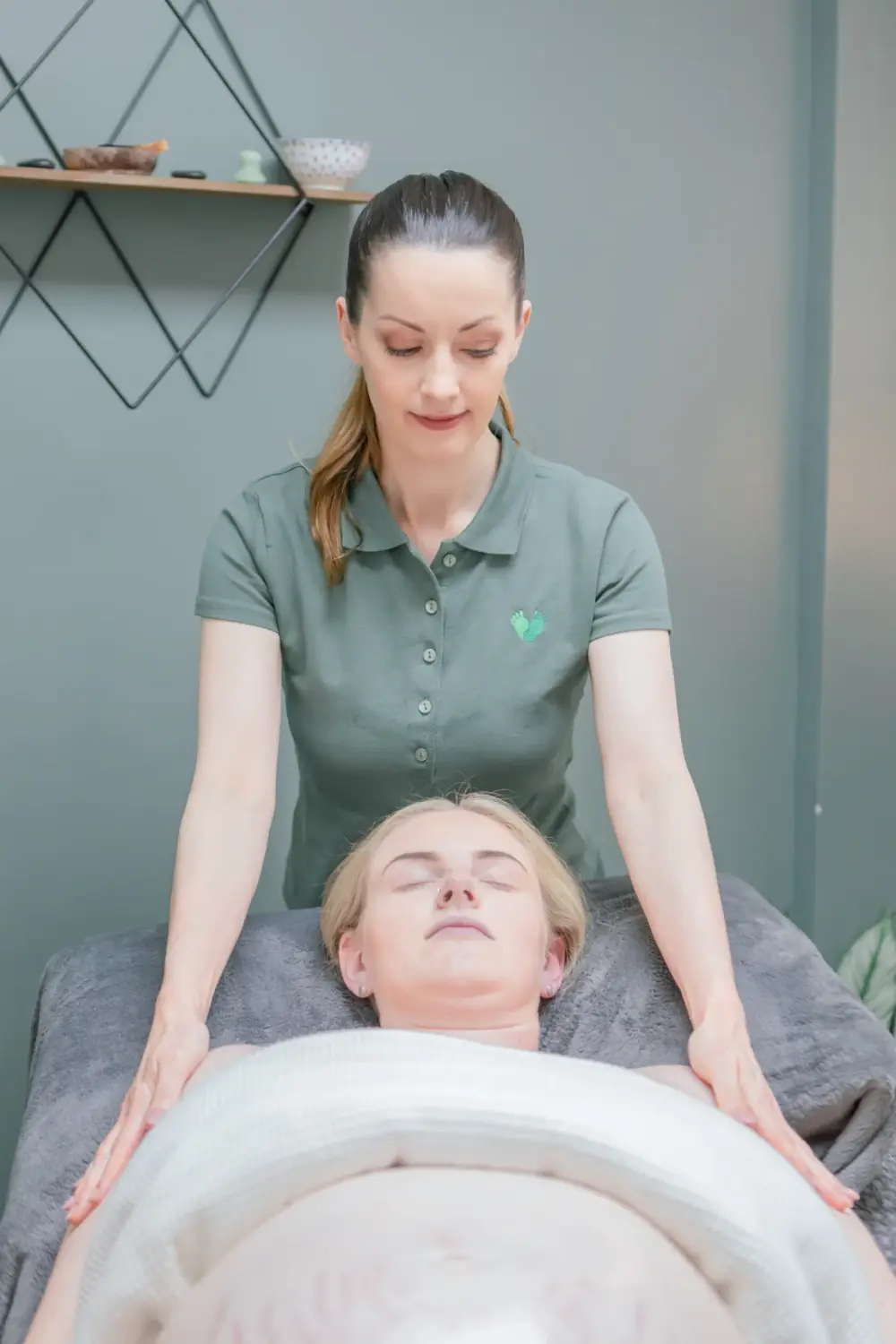 Massage therapist standing at the head of the couch, gently massaging a relaxed client’s neck and shoulders