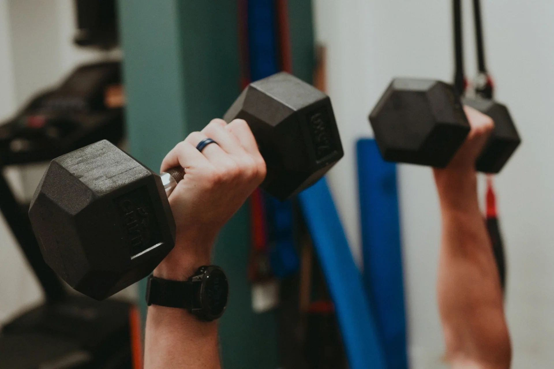 Close-up of a client pressing two hexagonal dumbbells overhead in the Exeter movement studio