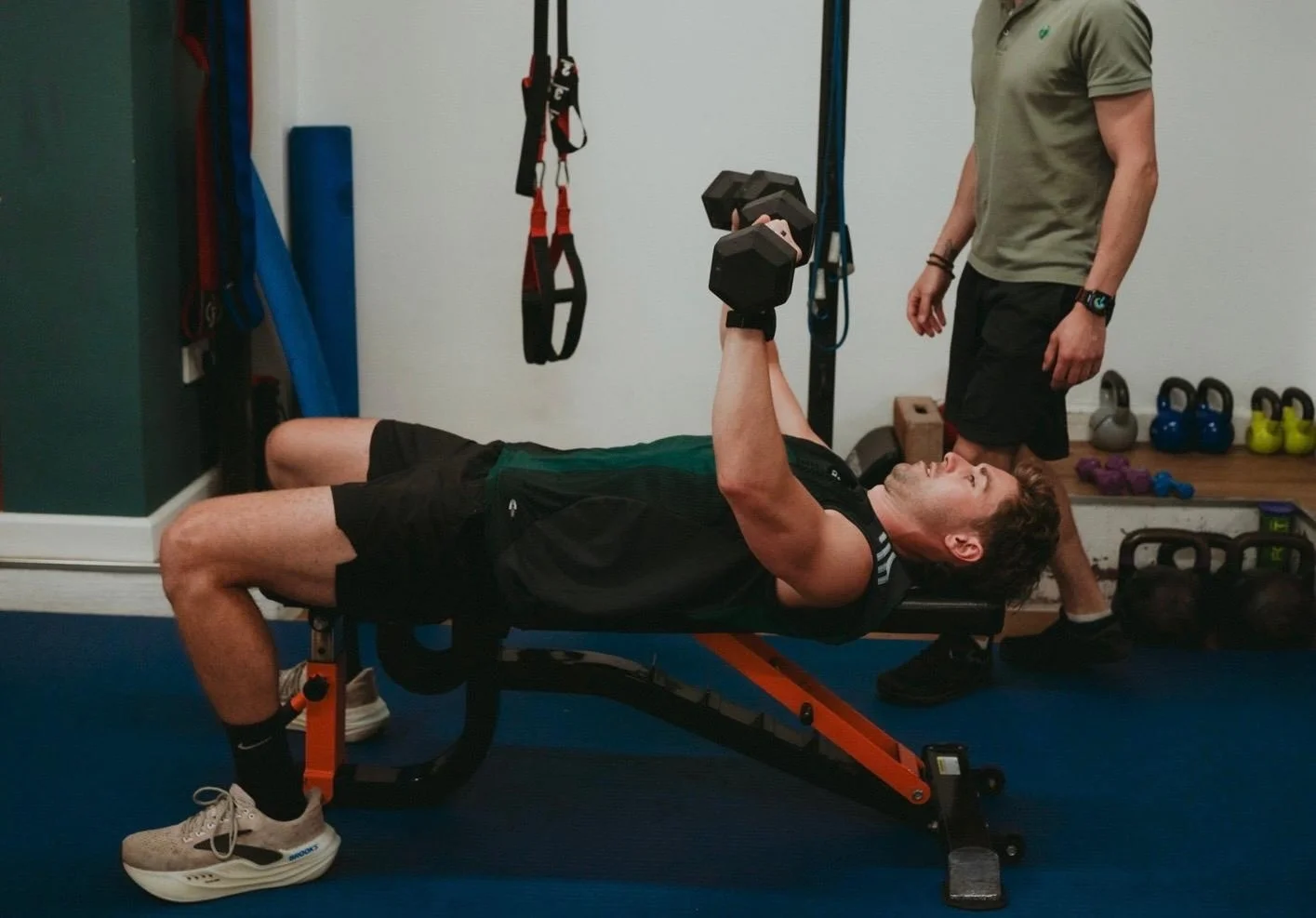 Coach watching a client press a pair of dumbbells on a weight bench in the Exeter movement studio