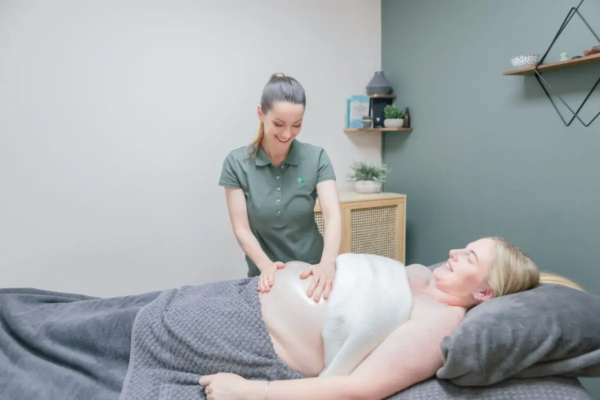 Massage therapist smiling as she gently massages a pregnant client lying comfortably on the treatment couch