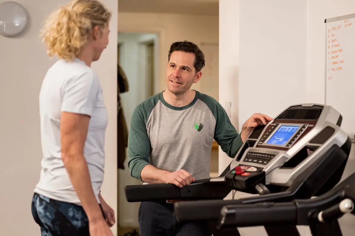 Physiotherapist at a treadmill console talking with a runner before her gait analysis in the Exeter studio