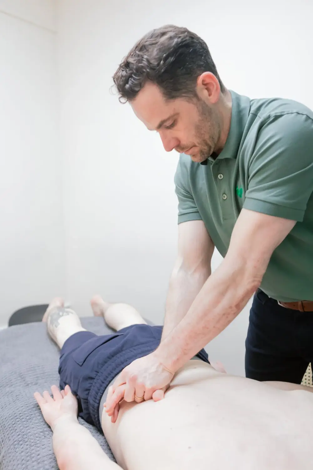 Therapist in a Barefoot polo giving hands-on treatment to a client’s lower back on the treatment couch