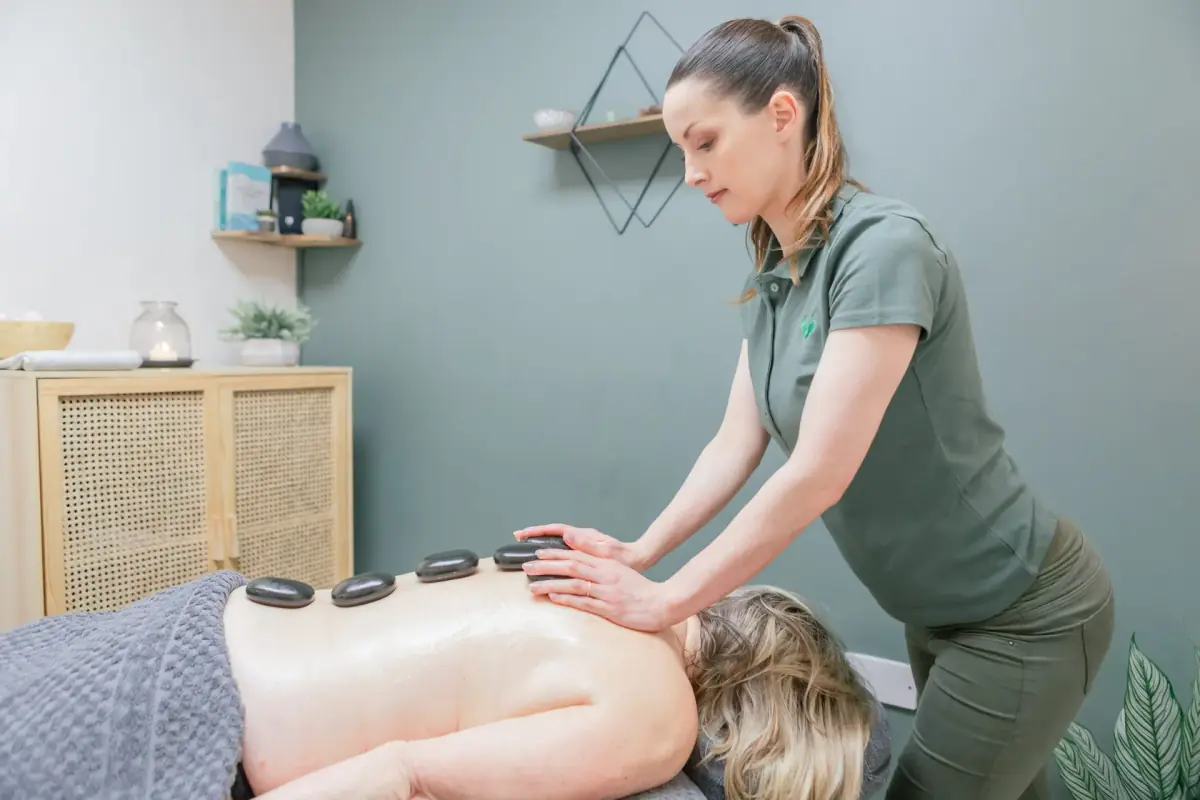 Massage therapist working along a client’s back with a line of smooth heated basalt stones placed down the spine