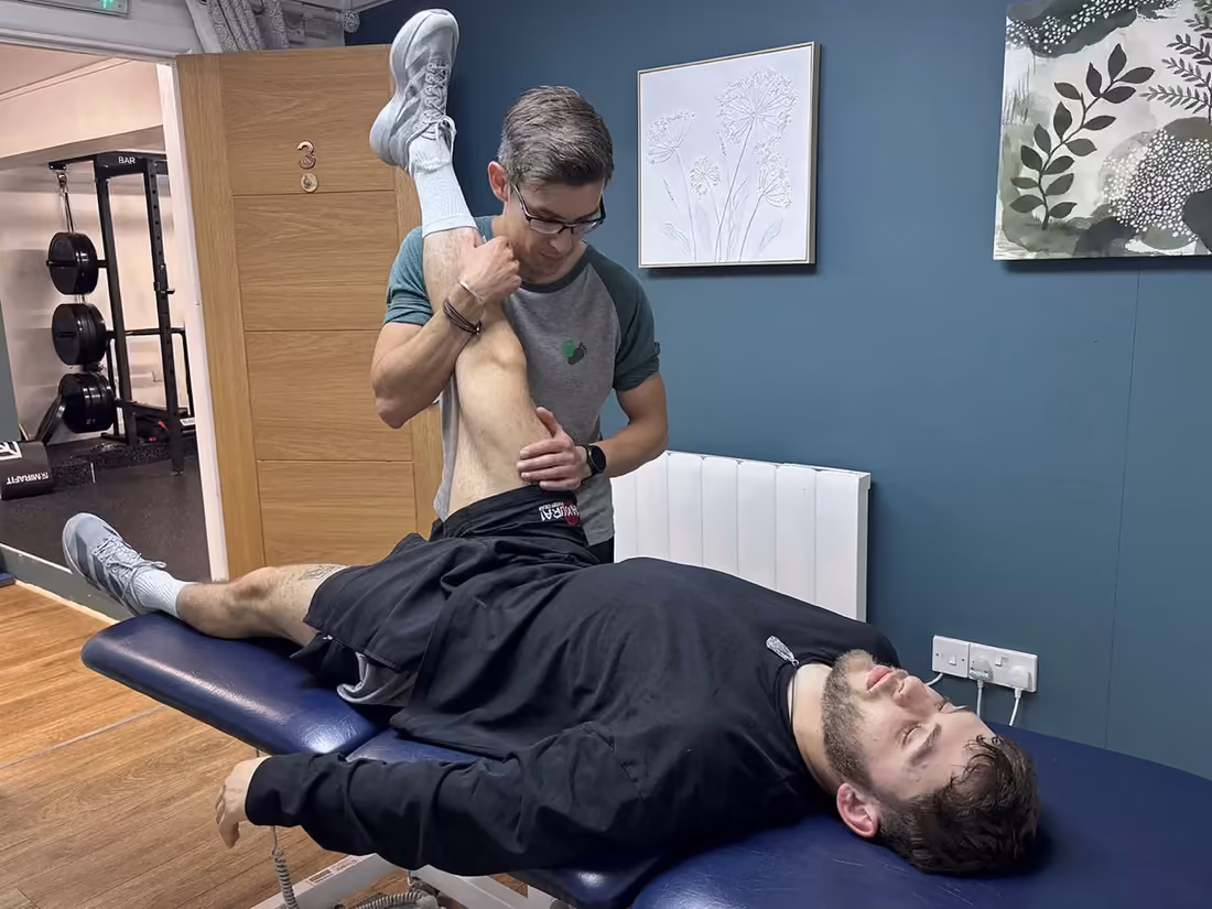 Therapist lifting and stretching a client’s leg as he lies relaxed on a treatment couch in the Barefoot studio